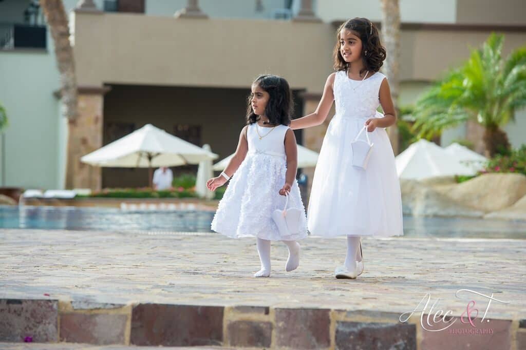  two girls that are flower girls dressed in white. 